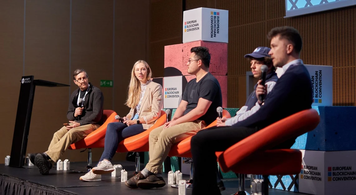 Five speakers seated on stage in a blockchain conference panel discussion